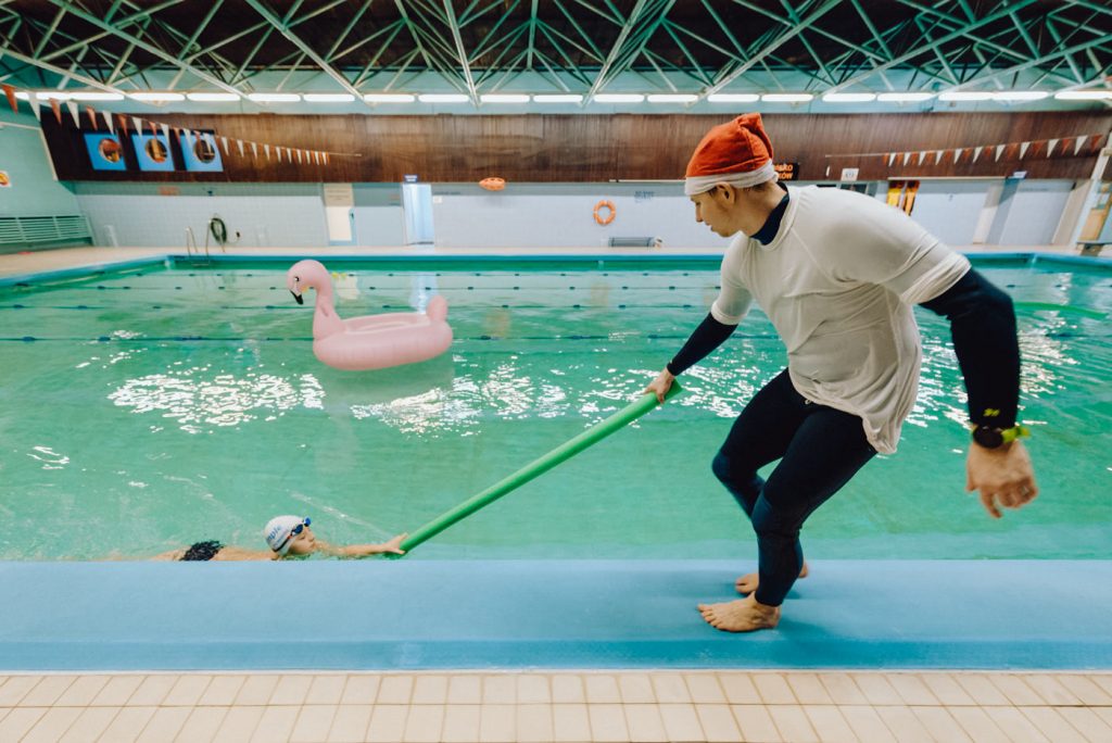A swimming instructor in a Santa hat pulls a boy in the water
