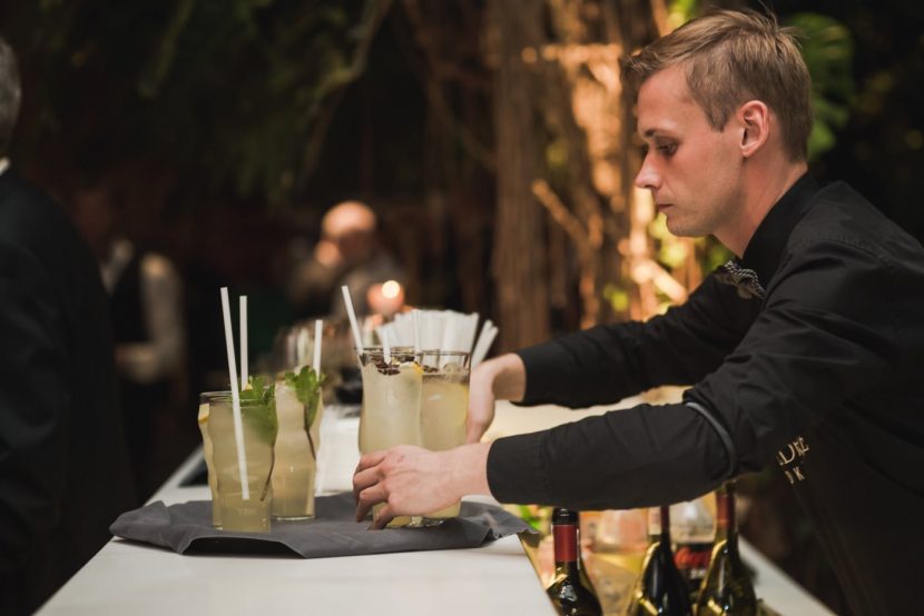 A bartender in a black shirt serves cold colored drinks on a tray