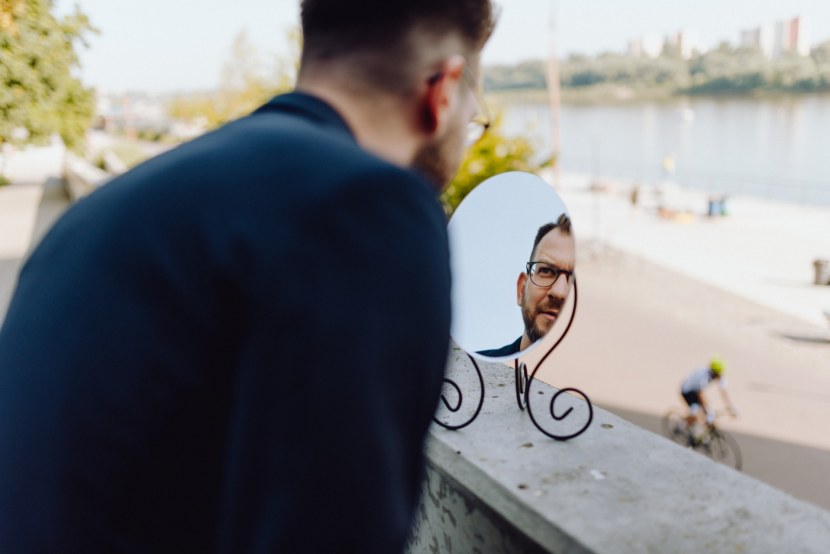 A man with glasses looks in the mirror