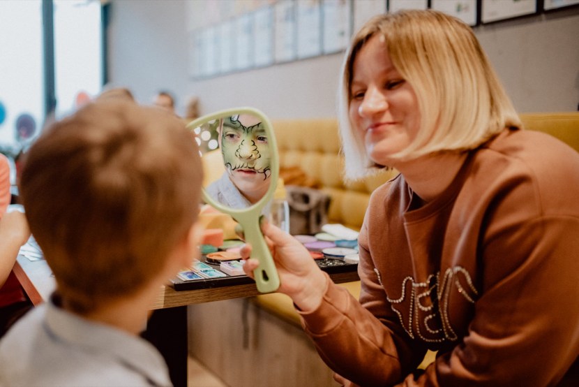 A woman holds a mirror in which the boy polishes his painted face
