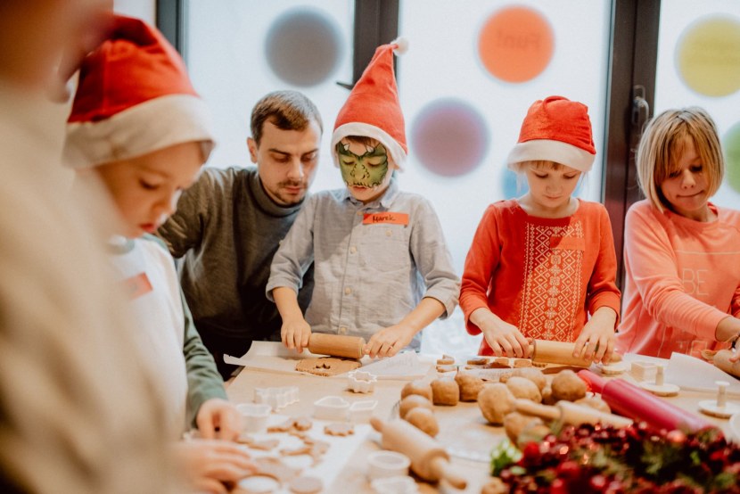 Dziecko z pomalowaną twarzą w czapce mikołaja robi z tatą pierniczki świąteczne