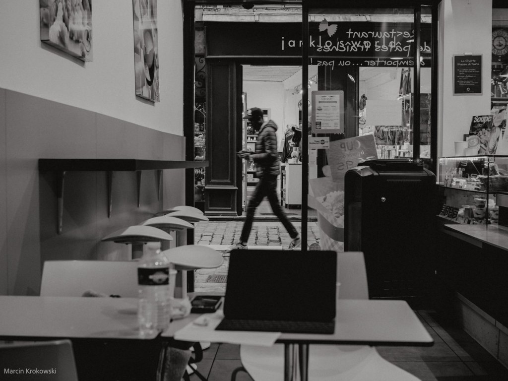 Black and white photo from inside a café of a passing man