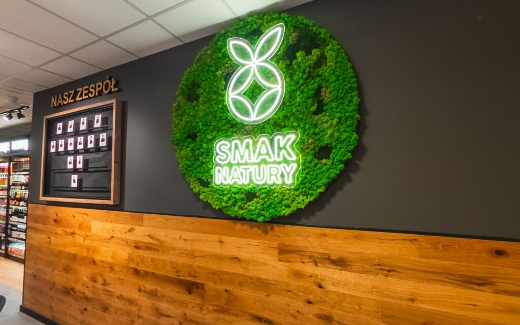 Virtual walk through the organic grocery store Smak Natury 2 - Urbanflavour.pl Checkout area in the Smak Natury store with the illuminated moss logo on the wall
